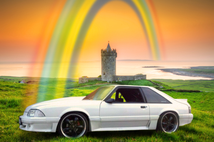 St Patricks themed image with a car on a green grass landscape with rainbow above and a castle in the background